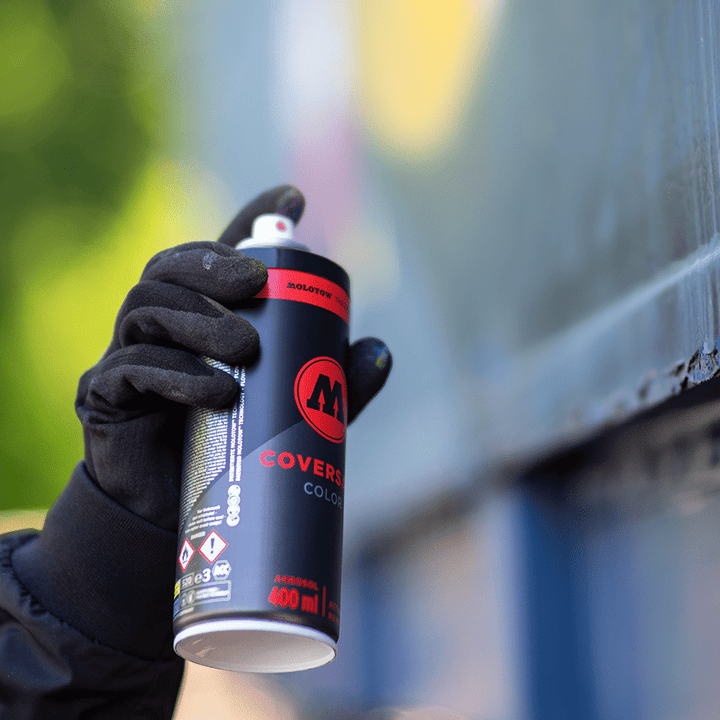 MOLOTOW COVERSALL Color 400ml spray can, black with red logo, held by a gloved hand, actively spraying.