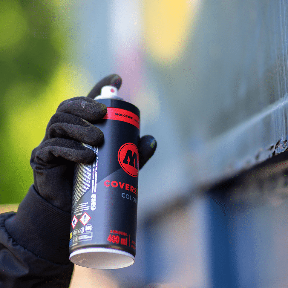 MOLOTOW COVERSALL Color 400ml spray can, black with red logo, held by a gloved hand, actively spraying.