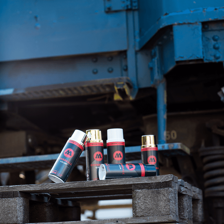 Cinque bombolette spray MOLOTOW COVERSALL Color 400ml in nero, bianco, oro e cromo su pallet di legno.