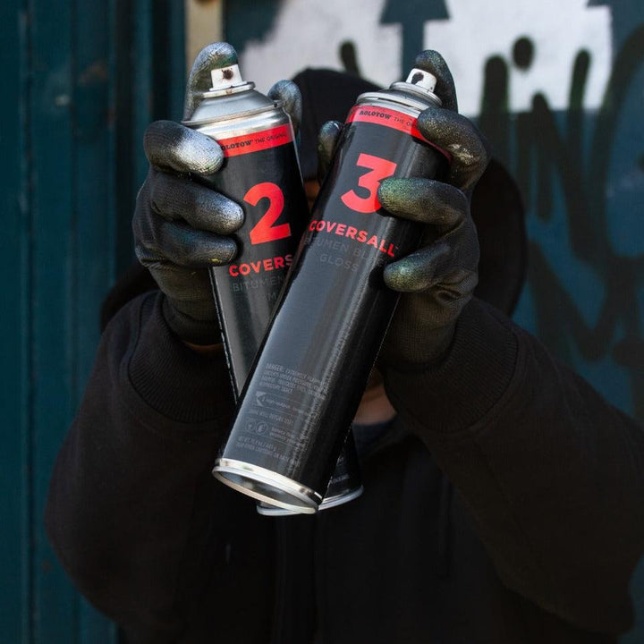 MOLOTOW™ COVERSALL™ Bitumen Spray 600ml cans, matte black with red "2" and "3" labels, held by gloved hands.